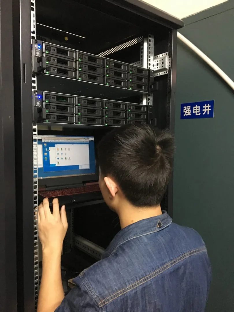 元禾大千艺术品有限公司机房实施照片,工程师在机柜前调试群晖 NAS 主备存储设备,多台机架式 NAS 硬盘指示灯正常运行,体现企业文件中心部署与现场实施交付
